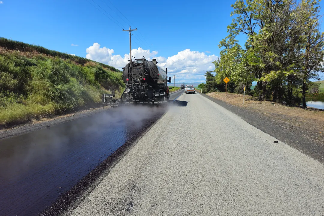 Pavimentadora extendiendo la capa asfáltica sobre la base granular de una vía rural